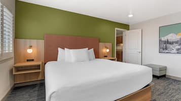 A hotel room with a large bed, bedside tables, a nightstand, a bench, a door, and a painting on the wall.