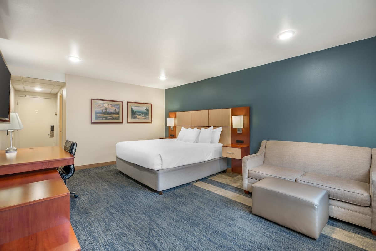 Ett hotellrum med en säng, ett skrivbord, en stol, en soffa och en liten pall.