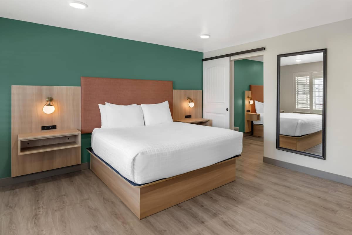 Ett modernt hotellrum med en stor säng, sängbord, en spegel och utsikt över omgivningarna.