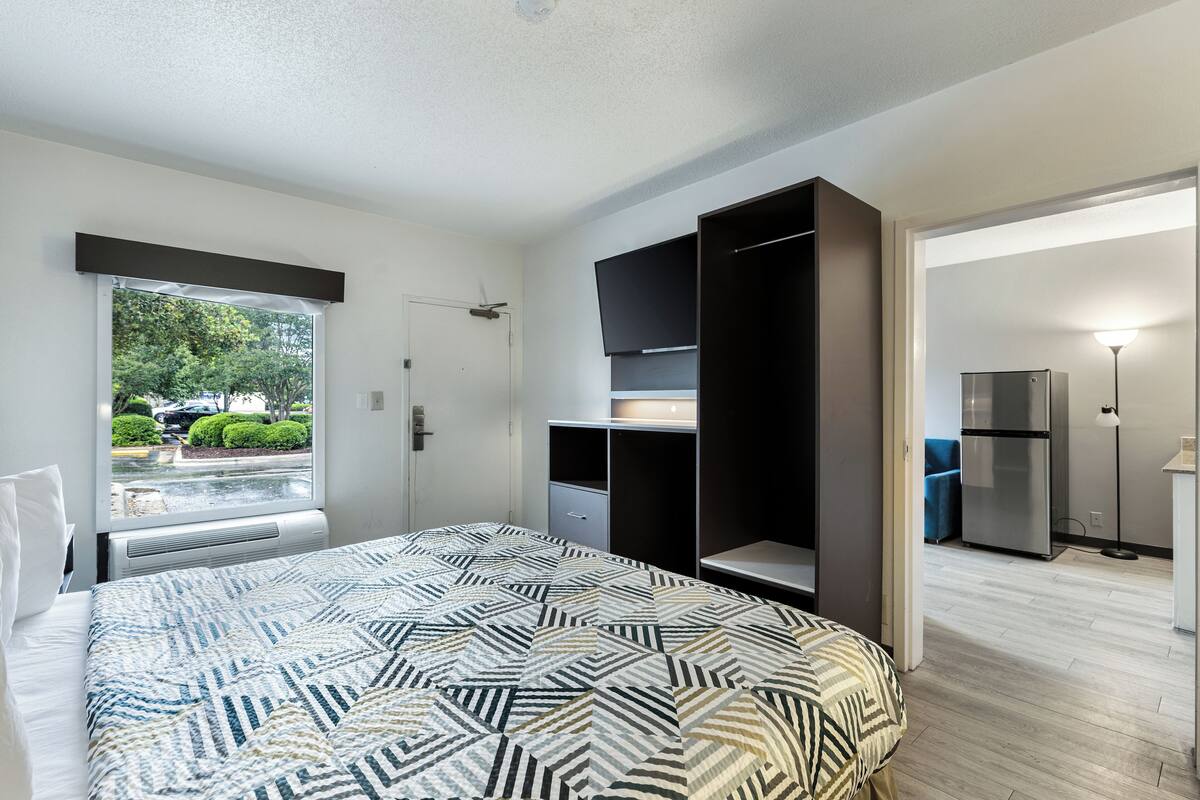 A bedroom with a bed, a wardrobe, a desk, and a view of the outside.