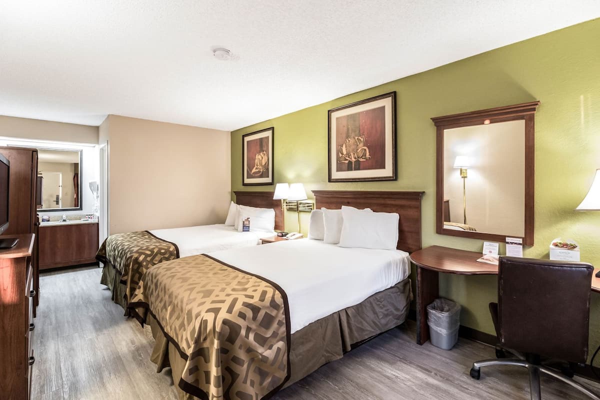 A hotel room with two beds, a desk, a chair, a trash bin, and a mirror.
