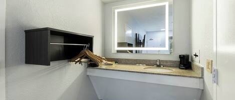 Un baño moderno con un lavamanos blanco, un espejo con iluminación integrada, un armario de baño de madera oscura y una cafetera sobre la encimera.