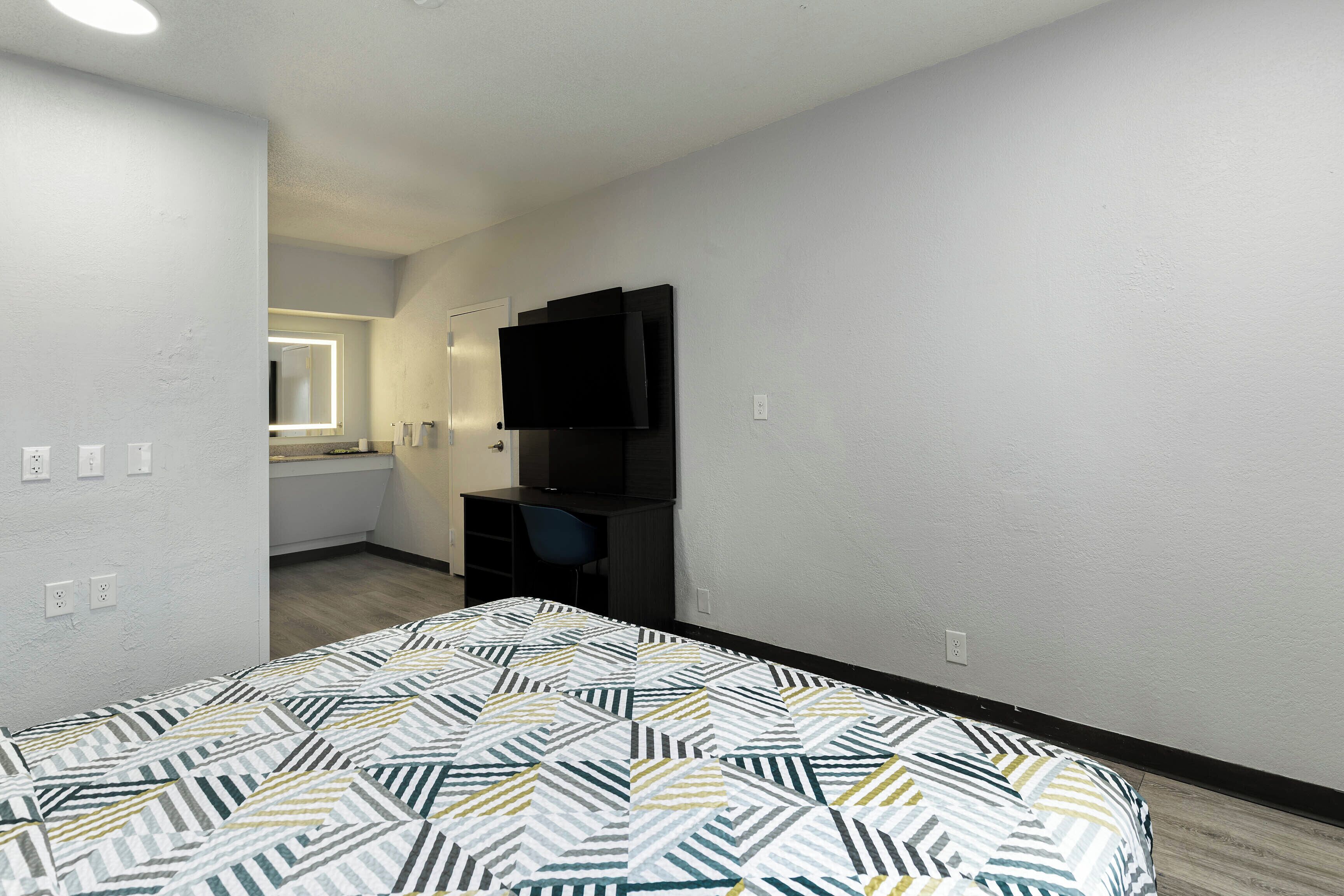 Un dormitorio con una cama, un escritorio, una silla, un televisor y una ventana.