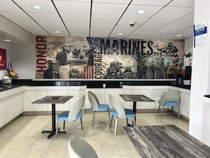 A restaurant interior with a counter, four chairs, and a wall mural depicting military scenes. - Studio 6 Suites Jacksonville, NC (Jacksonville)