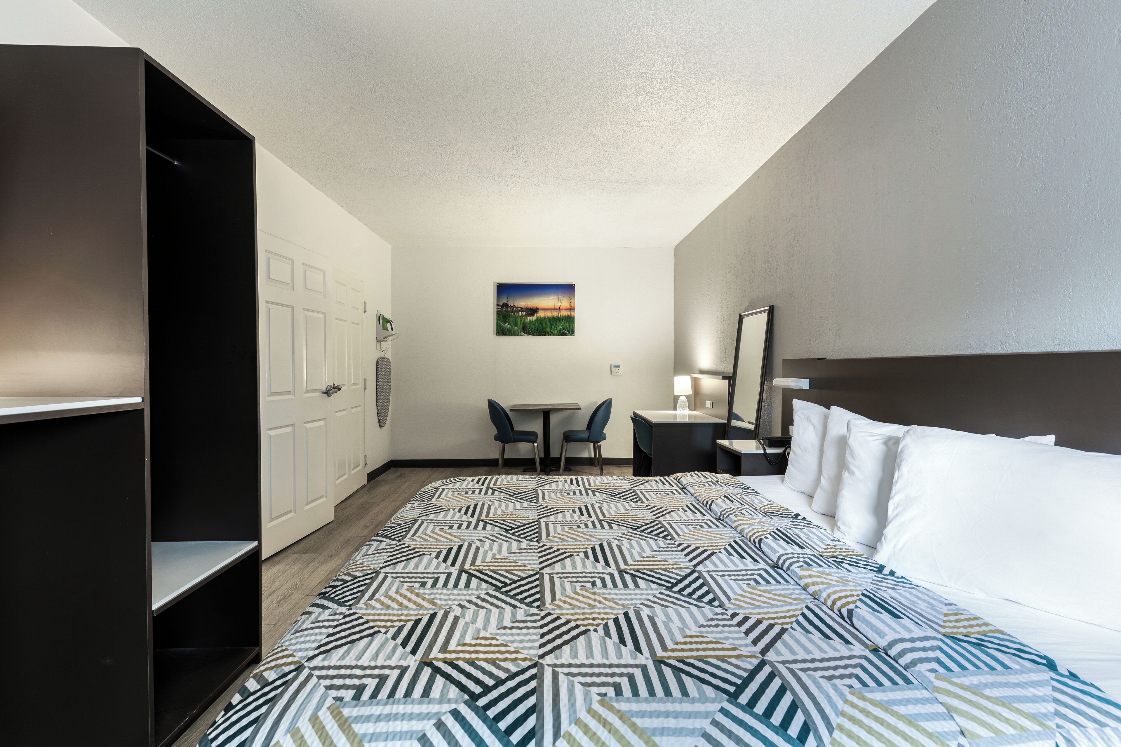 Habitación de hotel con cama, escritorio, dos sillas, una mesita, un cuadro en la pared y un armario.