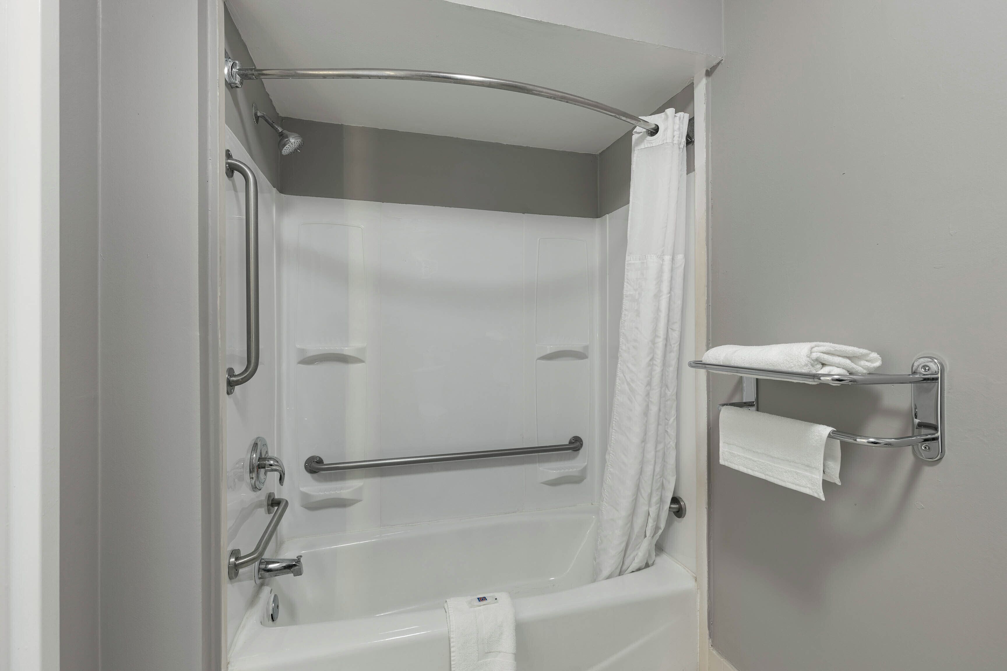 Un baño con bañera, barras de apoyo, cortina de ducha, toallero y toalla.