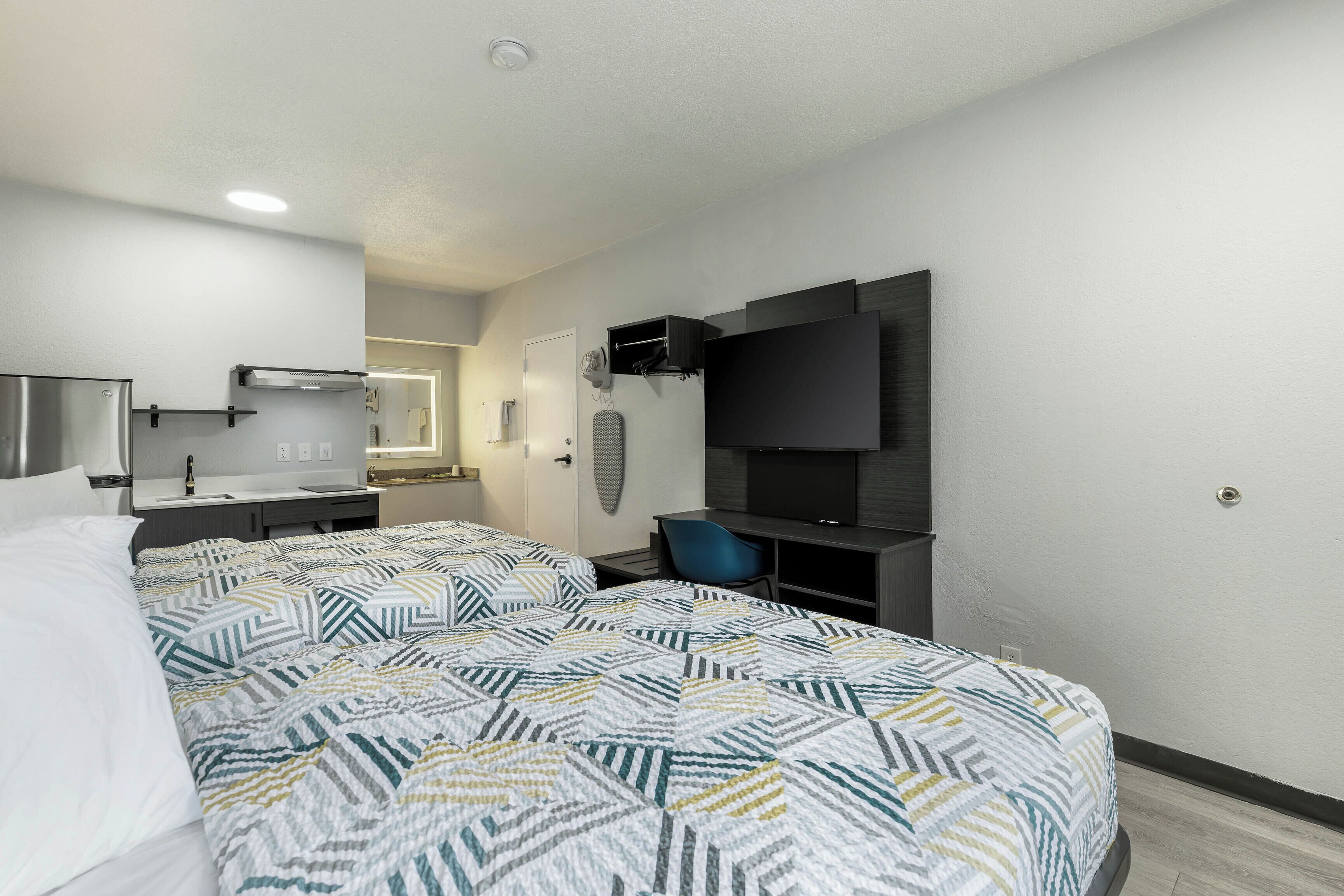 A hotel room with a bed, a desk, a chair, a TV, a mirror, and a bathroom.