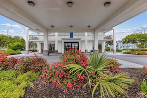 A gas station with a covered entrance, a blue door, and surrounding landscaped areas with various plants and flowers. - Studio 6 Suites Jacksonville, NC (Jacksonville)