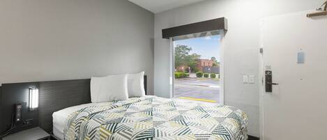 A hotel room with a bed, bedside table, and a door leading to a parking area.