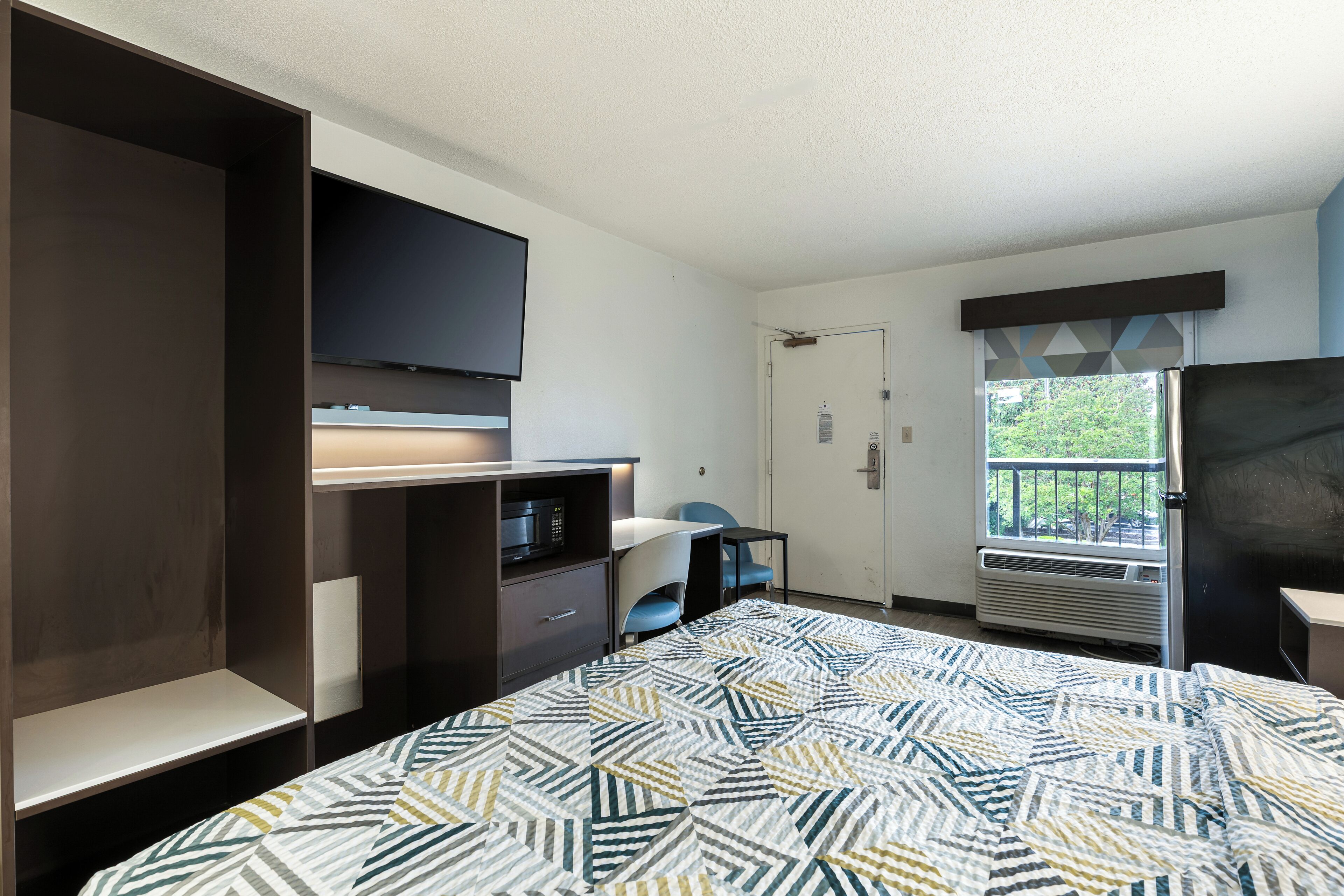 A bedroom with a bed, a TV, a desk, a chair, a wardrobe, and a window with a view.