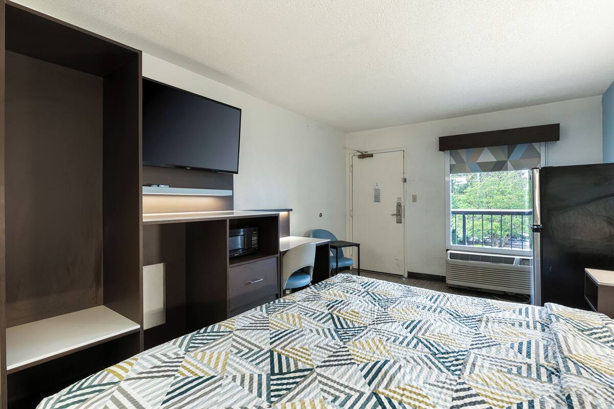 A bedroom with a bed, a TV, a desk, a chair, a wardrobe, and a window with a view.