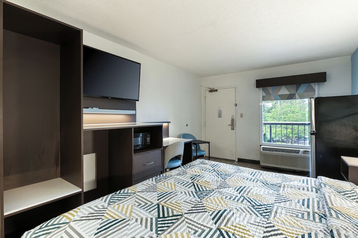 A bedroom with a bed, a TV, a desk, a chair, a wardrobe, and a window with a view.