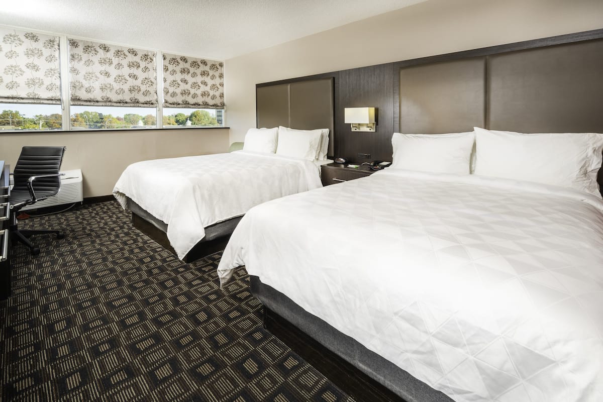 A hotel room with two beds, a desk, and a chair.