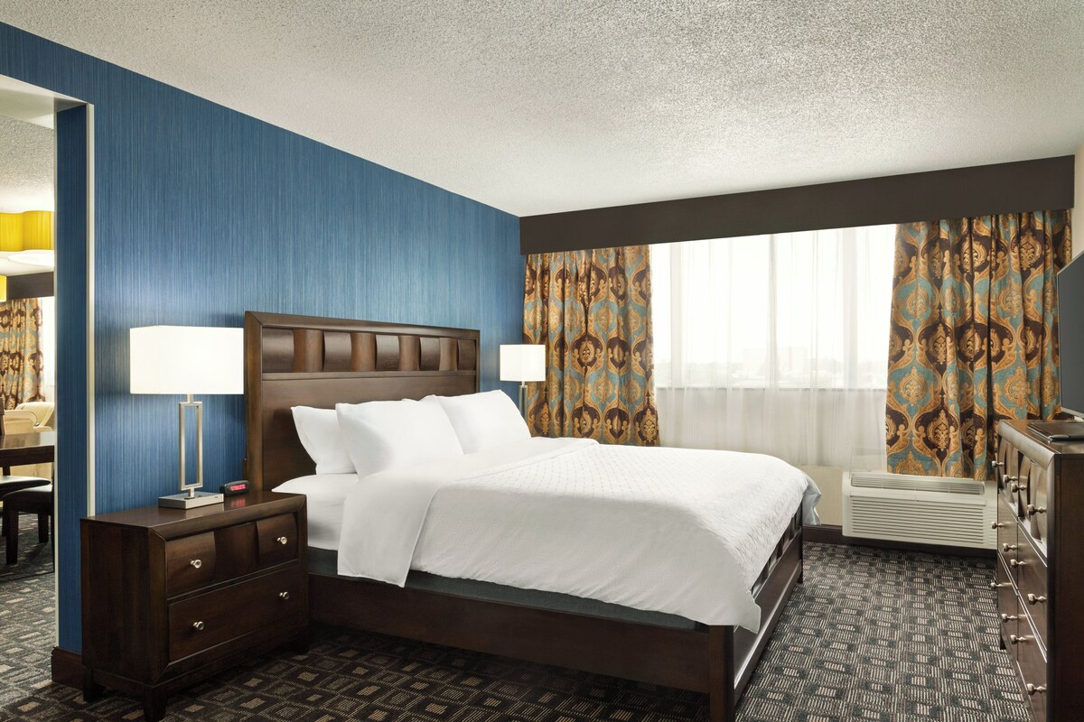 A hotel room with a large bed, a dresser, a desk, and a mirror.