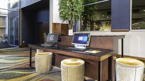 Un mostrador de recepción con dos computadoras, una planta y tres taburetes estampados.
