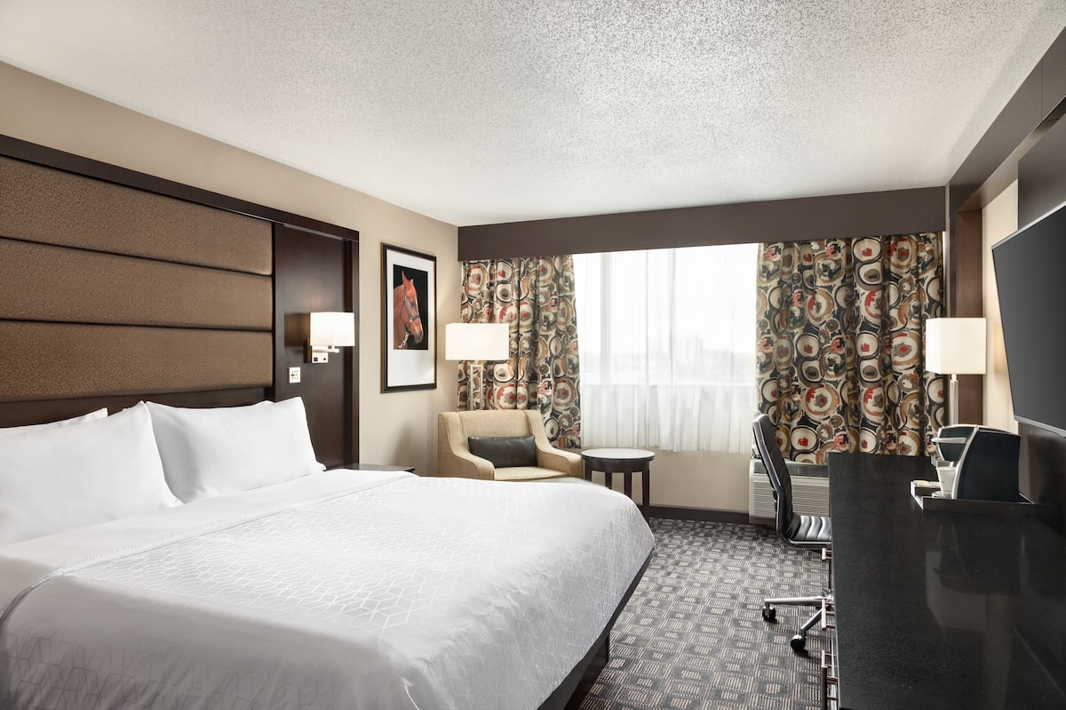 A hotel room with a large bed, a desk, a chair, and a TV.