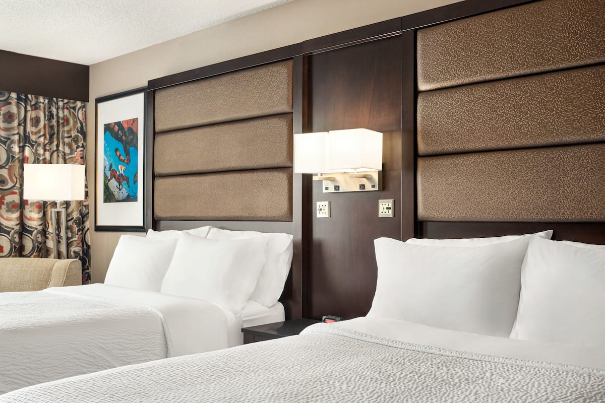 A hotel room with two beds, a large painting on the wall, and a nightstand with a lamp.