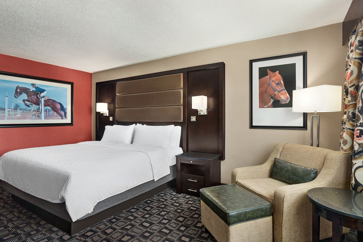 A hotel room with a large bed, a chair, a small table, and two wall-mounted lamps.