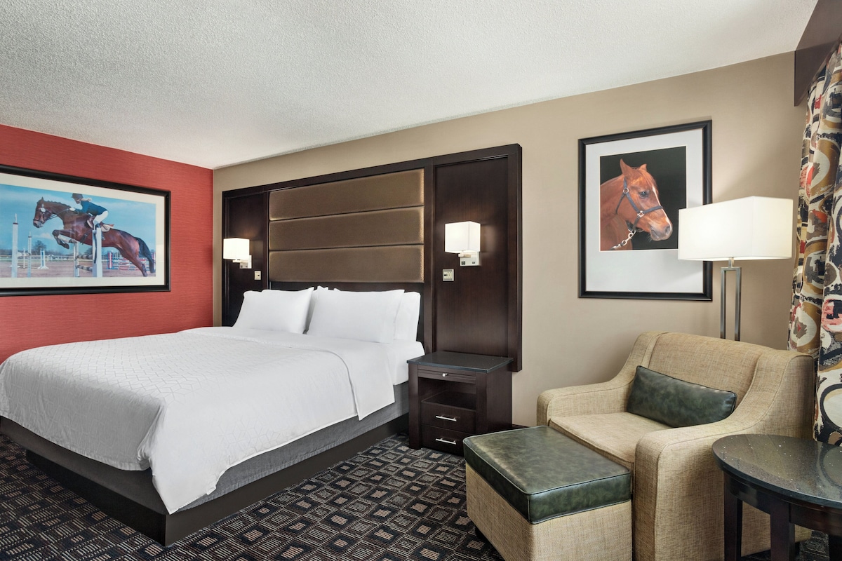 A hotel room with a large bed, a chair, a small table, and two wall-mounted lamps.