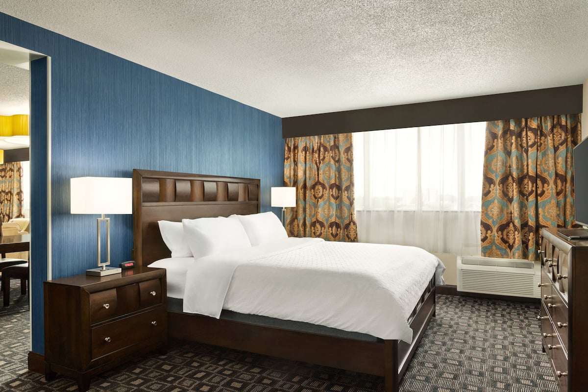 A hotel room with a large bed, a dresser, a desk, and a mirror.