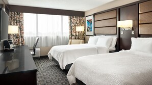 Habitación de hotel con dos camas, un escritorio, una silla, un televisor y una ventana con cortinas.
