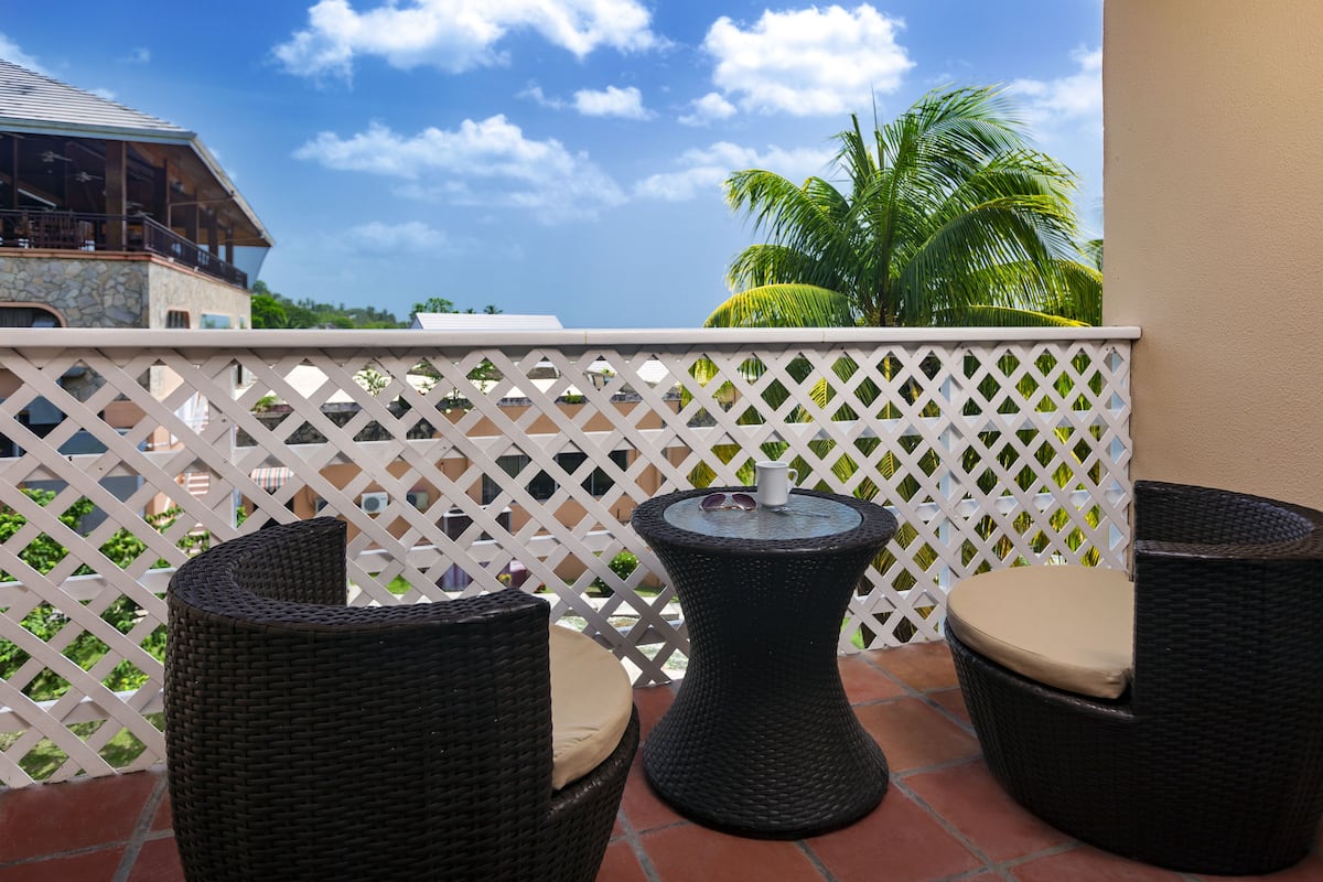 A balcony with wicker furniture and a small table, overlooking a building and palm trees.
