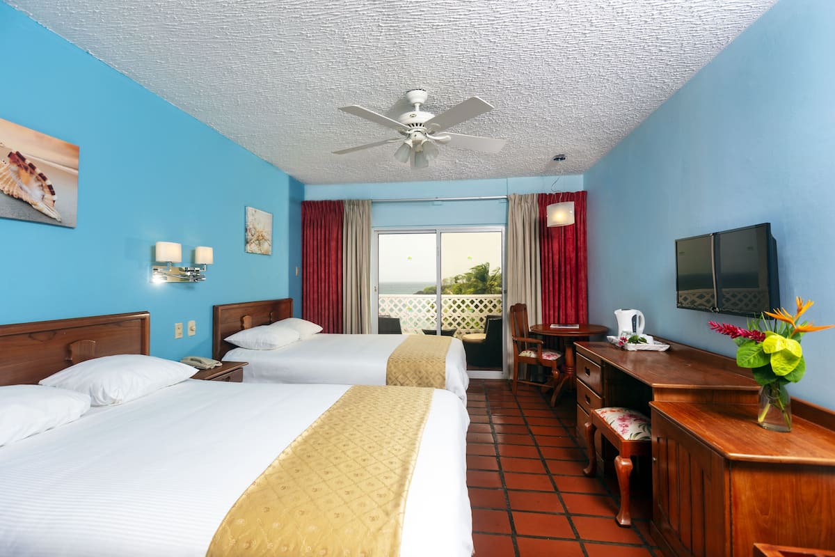 A hotel room with two beds, a desk, a chair, a television, and a balcony with red curtains.
