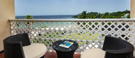 A balcony with wicker chairs and a small table, overlooking a beach and ocean.