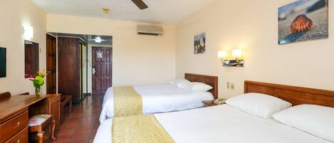 Habitación de hotel con dos camas, un escritorio, una silla, un ventilador de techo y un cuadro en la pared.