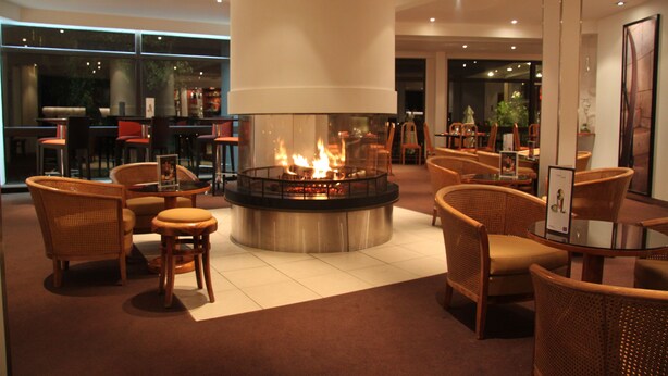Un espacio lounge moderno con una chimenea central, asientos cómodos y vistas al exterior.