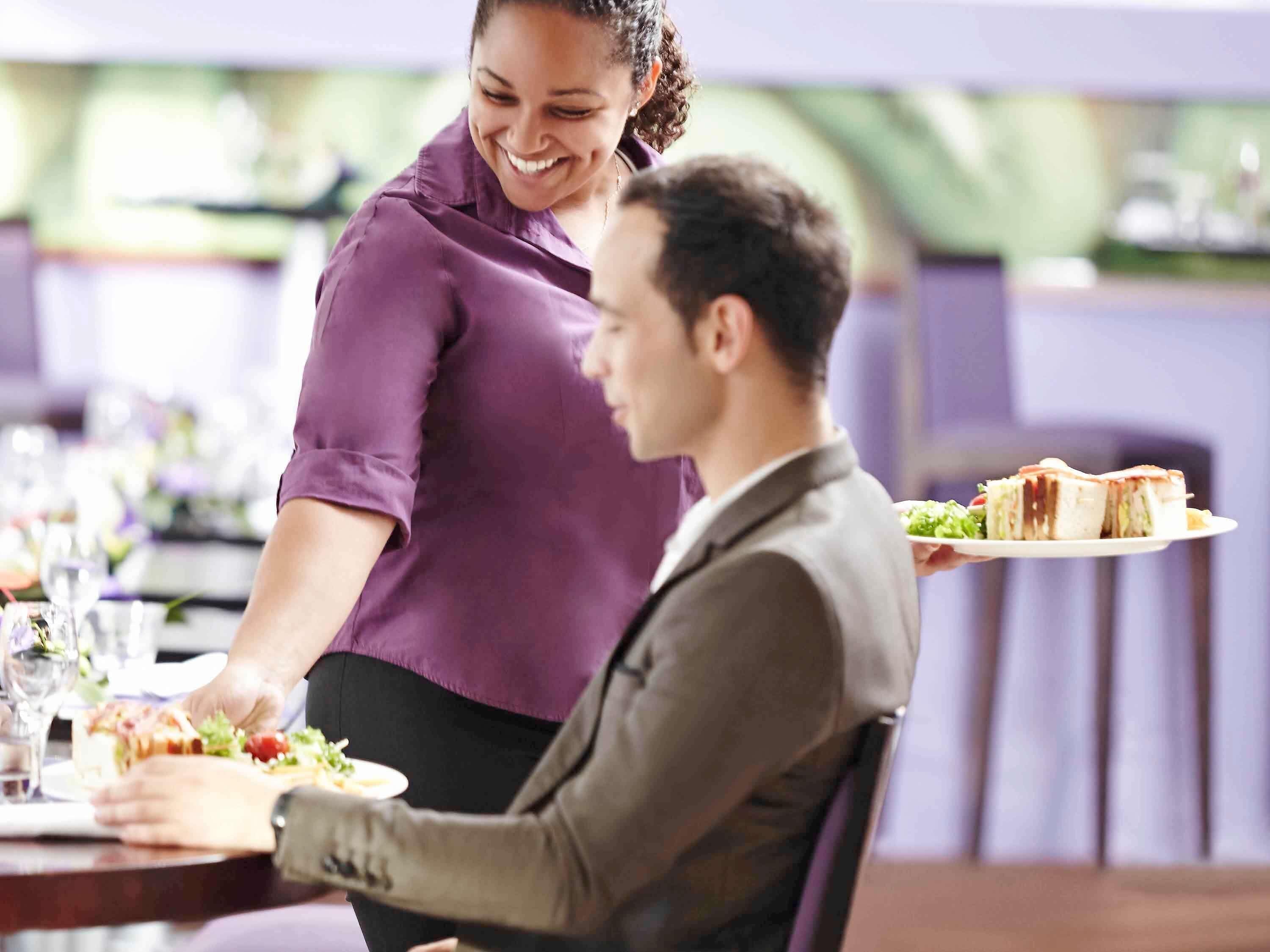 A restaurant setting with a dining table, chairs, and a person serving food.