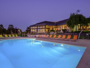 Una piscina con sillas de descanso, un edificio con grandes ventanales y cielo despejado.