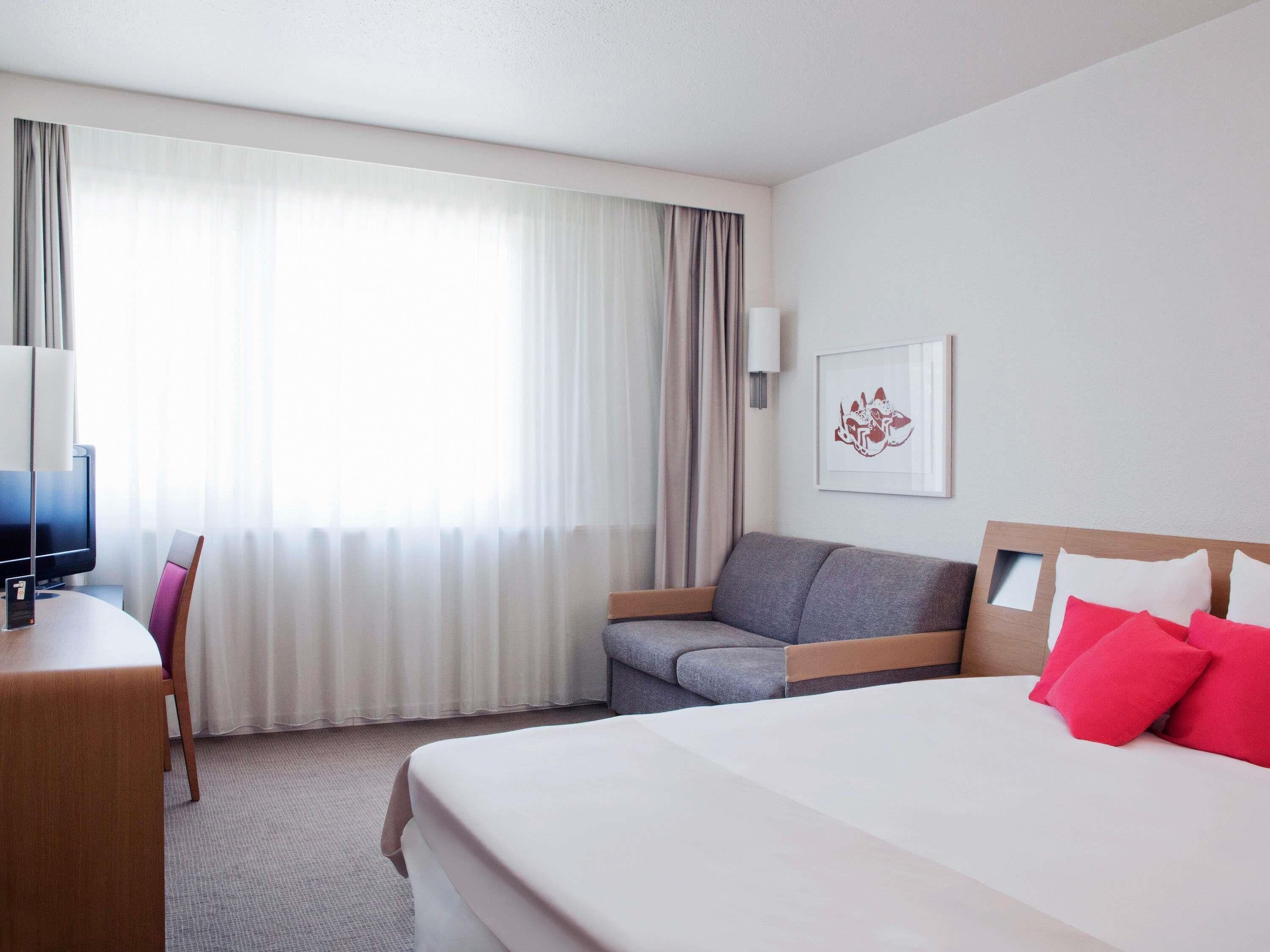 Une chambre d’hôtel avec un lit, un bureau, une chaise, un canapé et une fenêtre avec des rideaux.