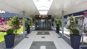 Una entrada moderna a un edificio con suelo de baldosas, un corredor cubierto y plantas en macetas.