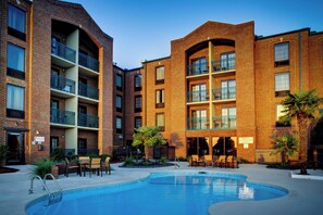A multi-story brick building with a swimming pool, outdoor seating, and balconies.