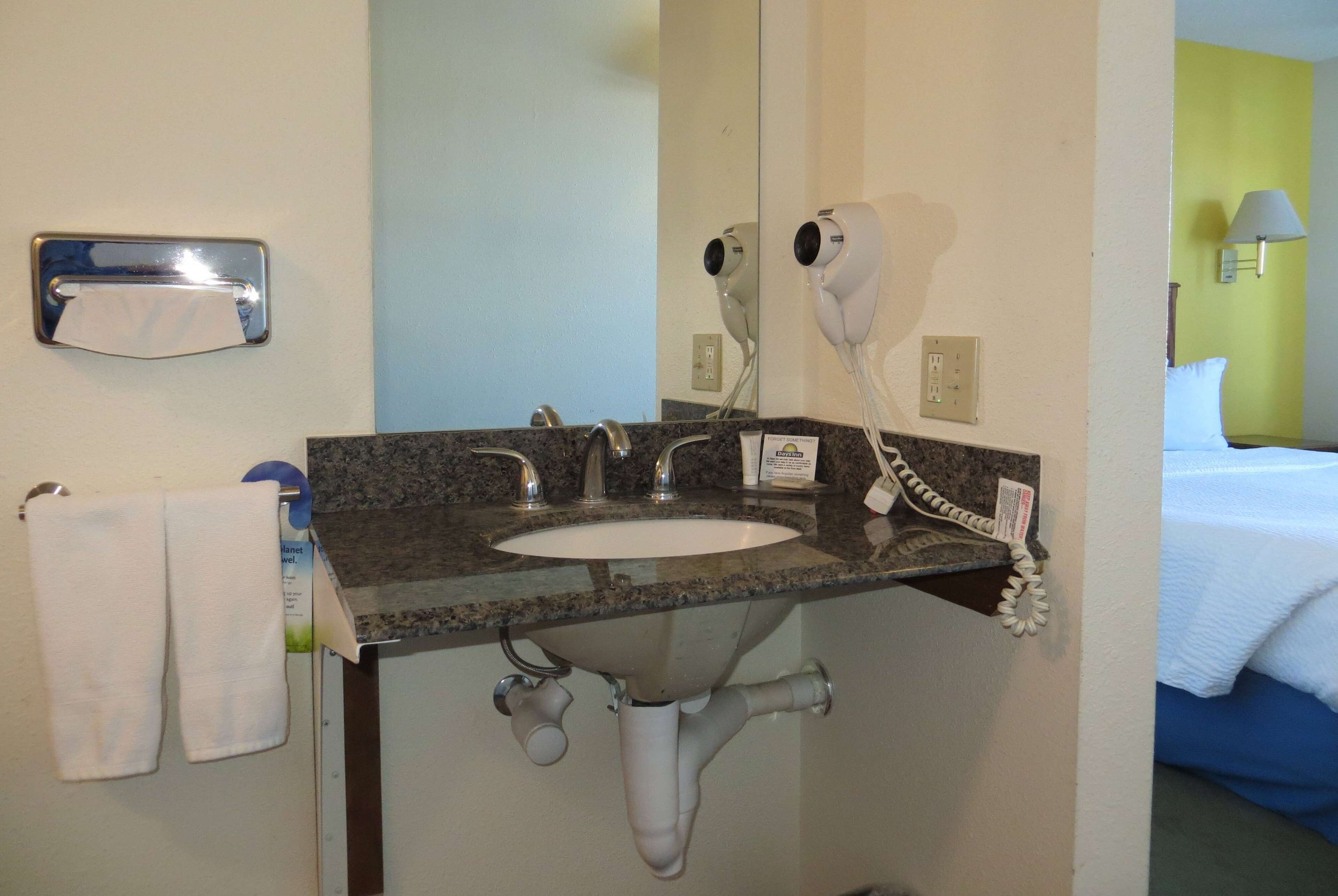 Casa de banho de hotel com uma pia, dois secadores de cabelo, um porta-toalhas e um telefone.