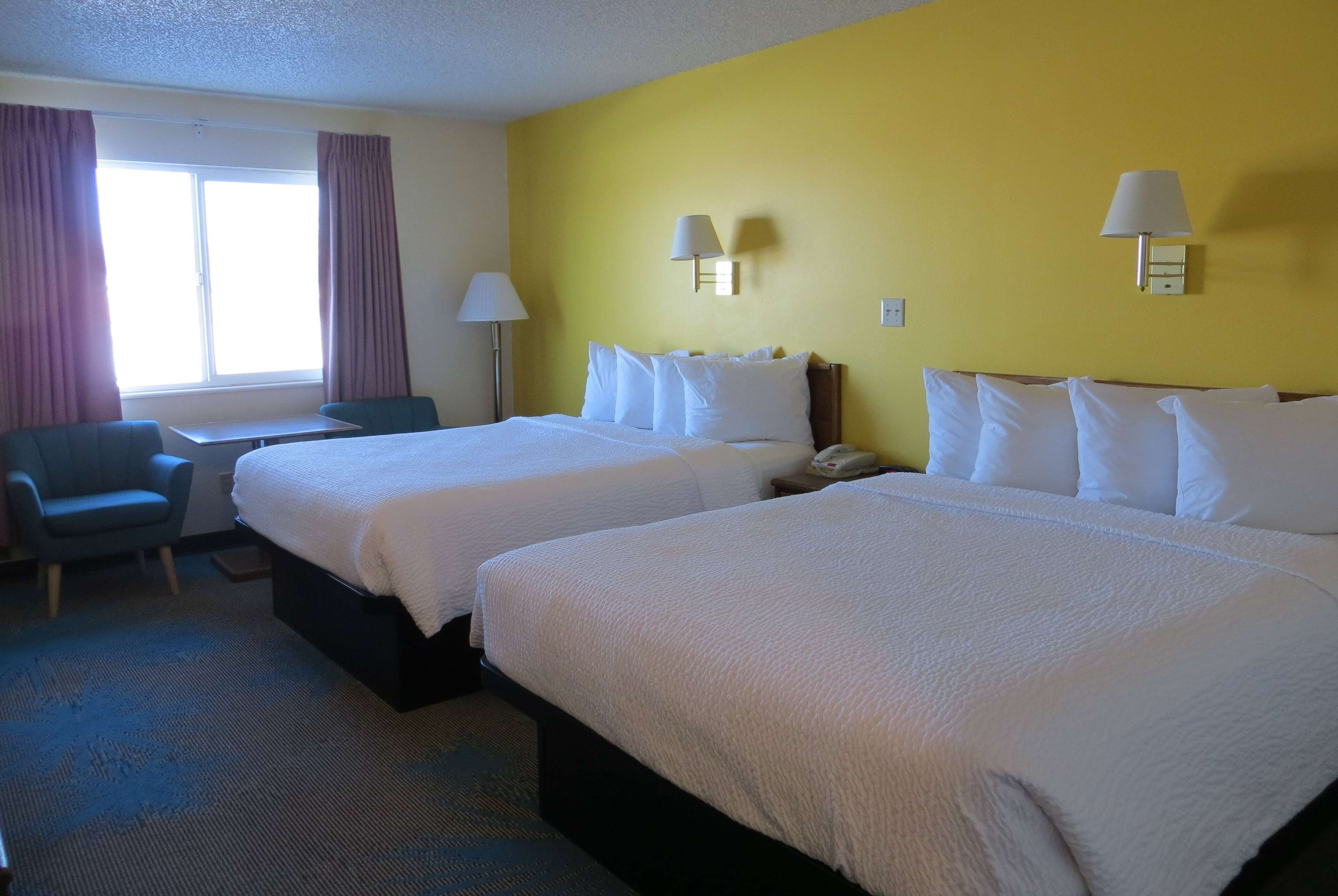 A hotel room with two beds, a desk, a chair, and a window with curtains.
