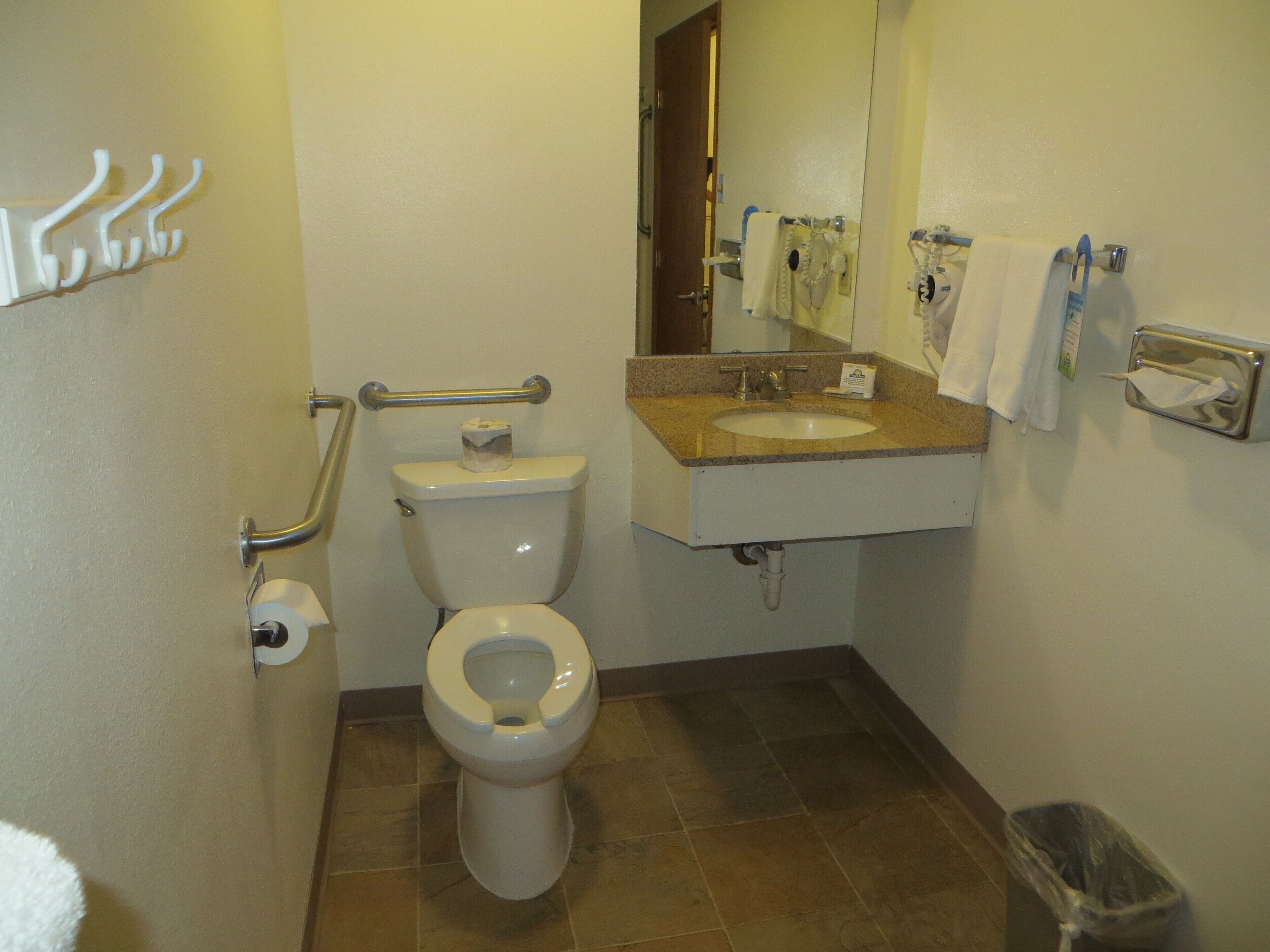 Un baño con inodoro, lavamanos y barras de apoyo.