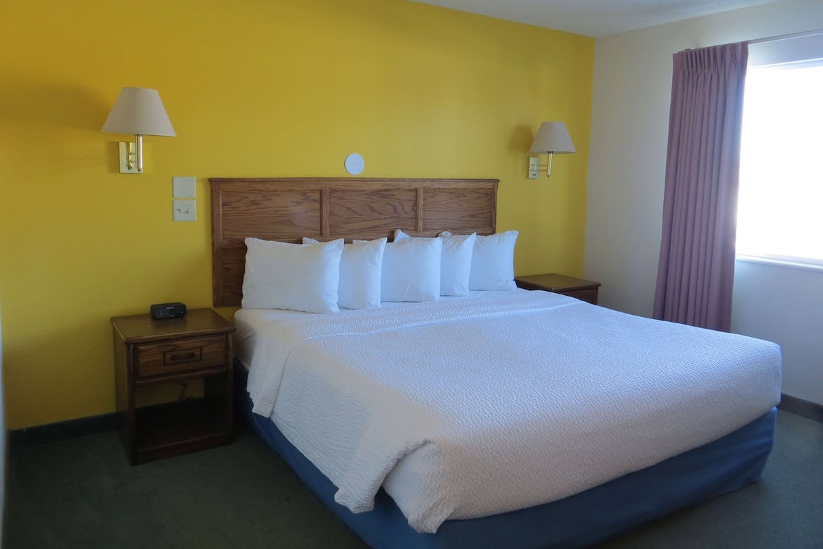 Una habitación de hotel con una cama grande, cabecera de madera, dos mesitas de noche y un atril.