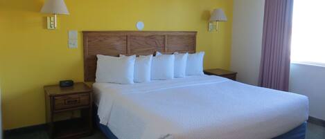 Una habitación de hotel con una cama grande, cabecera de madera, dos mesitas de noche y un atril.