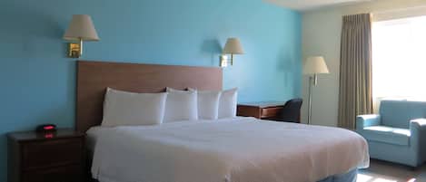 Una habitación de hotel con una cama grande, dos lámparas de noche, una mesita de noche con un reloj, una silla y una ventana con cortinas.