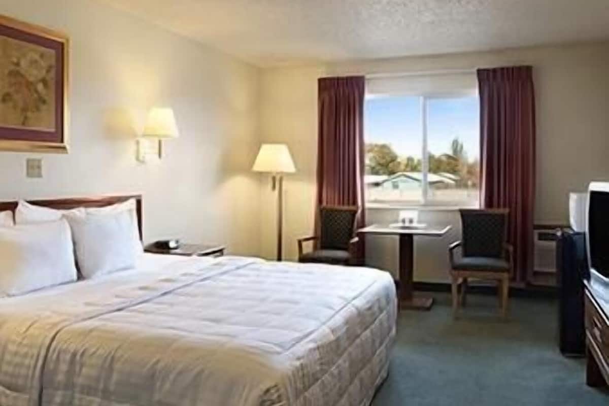 Habitación de hotel con cama, escritorio, silla, televisor y ventana con cortinas.