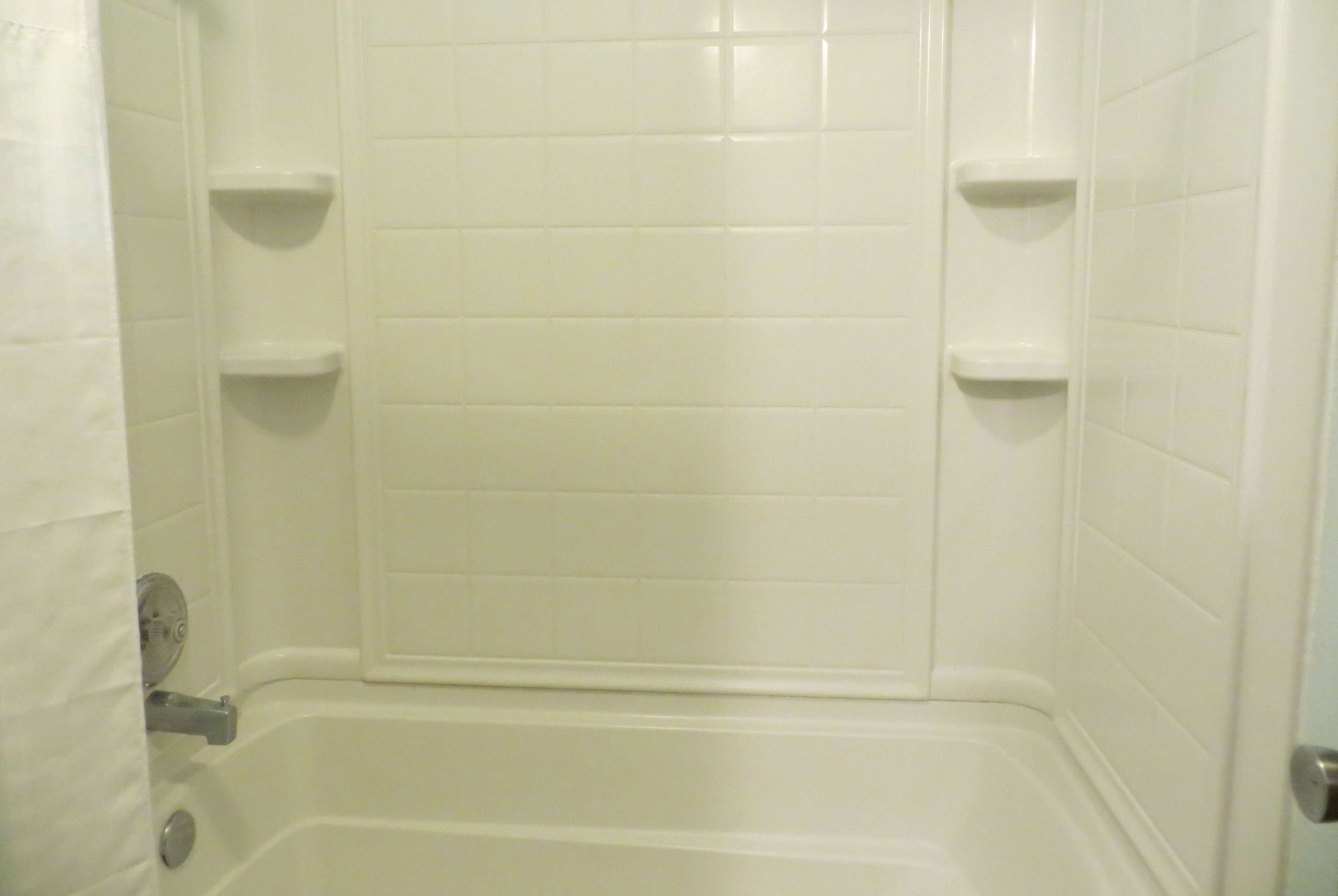 A bathroom with white tiled walls, a bathtub, and two small shelves.