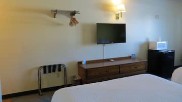 Habitación de hotel con cama, televisión montada en la pared, cómoda de madera, microondas y cubo de basura.