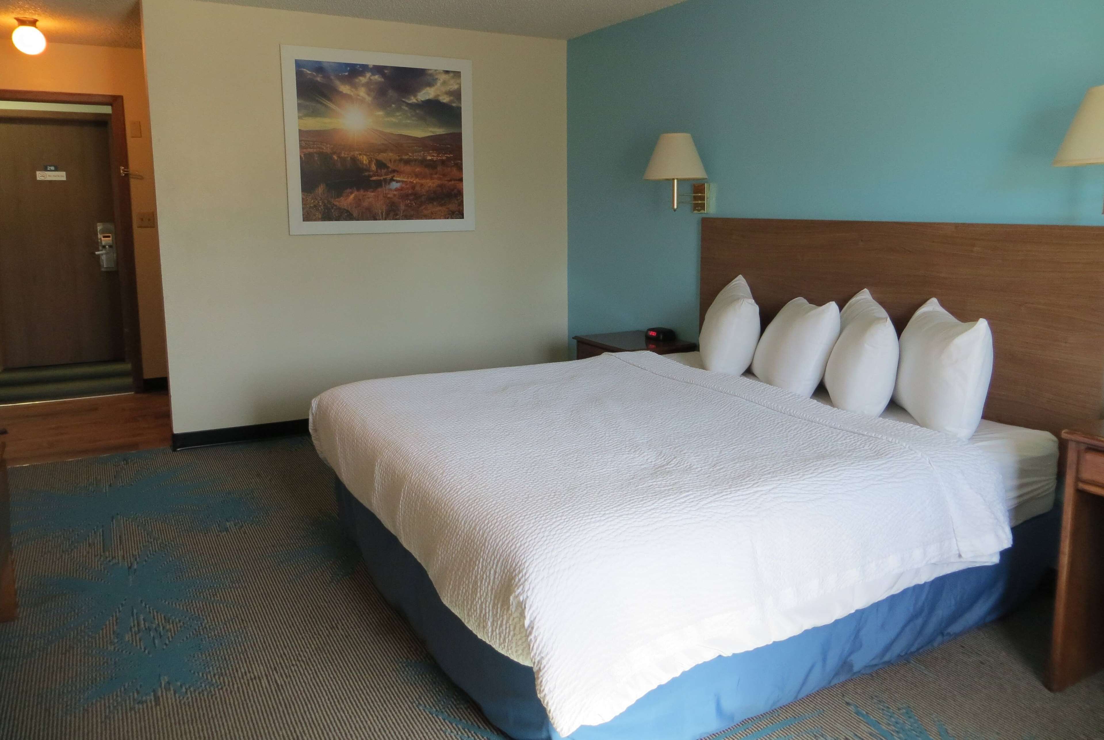 Una camera d'albergo con un letto grande, un comodino, una lampada a parete e una porta.