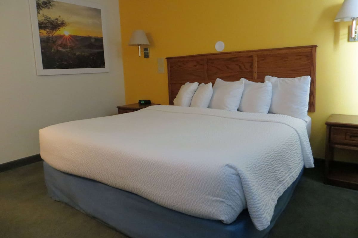 Una cama bien hecha con cubrecama blanco y falda azul, cabecera de madera y mesita de noche con lámpara.