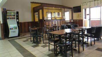 A restaurant with checkered flooring, wooden tables and chairs, a vending machine, and a counter with a television above it.