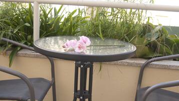 A round glass table with a metal base, surrounded by metal chairs, set against a wall with green plants.
