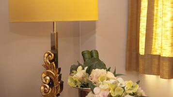 A lamp with a gold base and a yellow shade, a floral arrangement, and a window with curtains.