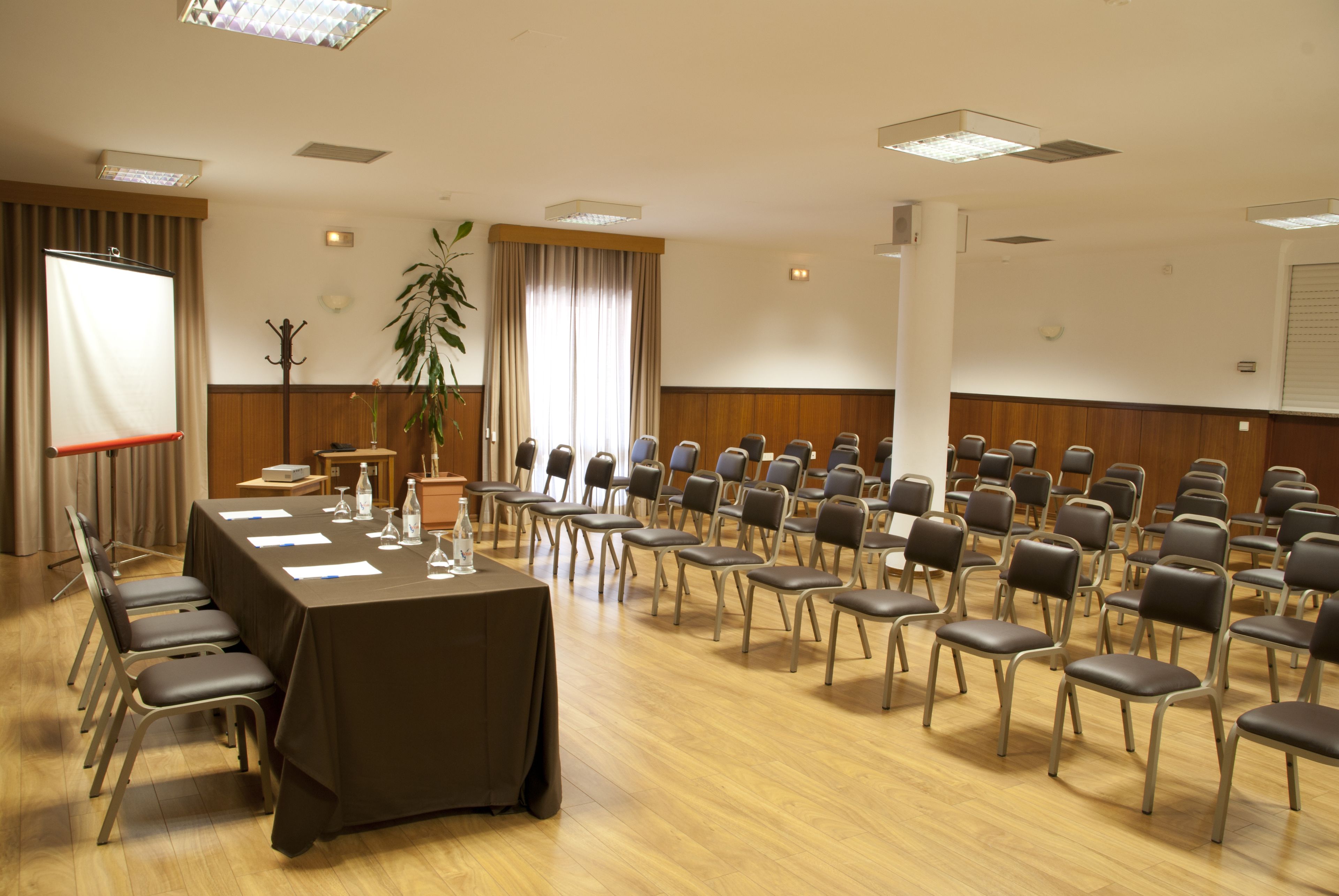 Un salón de conferencias con una mesa larga, sillas y una planta.